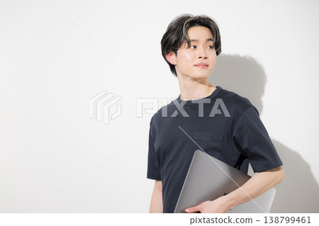 一位年輕的自由職業工程師或設計師,手持筆記型電腦,回頭望向前方,背景為白色。 一位年輕的自由職業工程師或設計師,手持筆記型電腦,回頭望向前方,背景為白色。 138799461