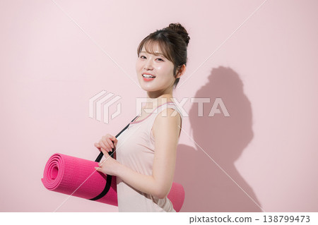 A woman with a yoga mat against a pink background, representing a healthy and beautiful lifestyle of training in sports at the gym or lifestyle. 138799473
