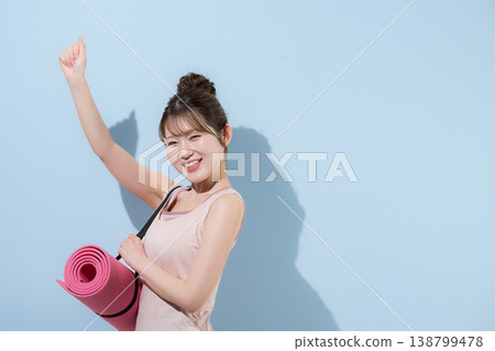 畫面中，一位女性在淺藍色背景下，鋪著瑜珈墊，正在健身房進行訓練，展現了她健康優美的體態。 138799478
