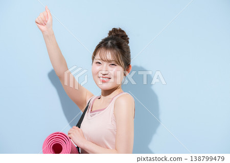 畫面中，一位女性在淺藍色背景下，鋪著瑜珈墊，正在健身房進行訓練，展現了她健康優美的體態。 138799479