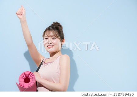 畫面中，一位女性在淺藍色背景下，鋪著瑜珈墊，正在健身房進行訓練，展現了她健康優美的體態。 138799480