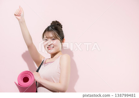 A woman with a yoga mat against a pink background, representing a healthy and beautiful lifestyle of training in sports at the gym or lifestyle. A woman with a yoga mat against a pink background, representing a healthy and beautiful lifestyle of training in sports at the gym or lifestyle. 138799481