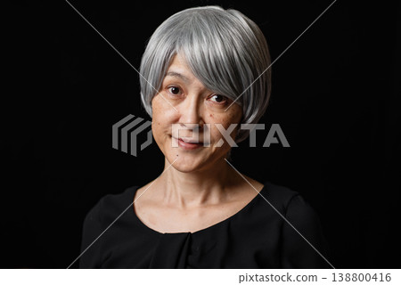 一位白髮蒼蒼的老婦人在黑色背景前微笑的肖像。 138800416