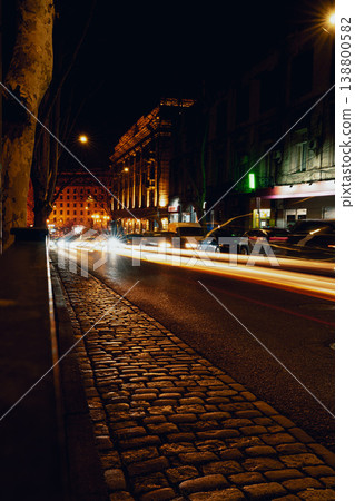Nighttime street scene with moving cars and glowing buildings in urban area 138800582