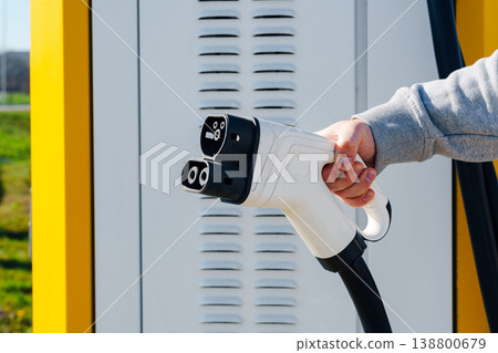 Electric car charger being held at a charging station in bright daylight 138800679