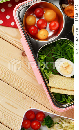 Lunch box with fresh vegetables, eggs, and cherry tomatoes arranged on a wooden table 138801262