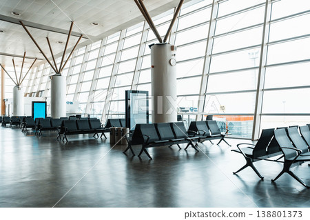 Waiting area in an airport during the day with large windows and empty seats Waiting area in an airport during the day with large windows and empty seats 138801373