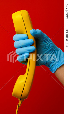 Holding a yellow phone with blue gloves in a red setting during a health crisis Holding a yellow phone with blue gloves in a red setting during a health crisis 138801379
