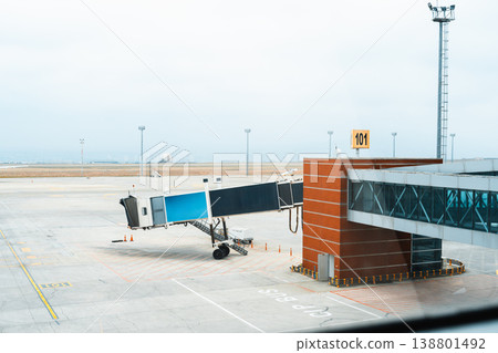 Plane boarding bridge is parked at gate 101 in an airport during a cloudy day Plane boarding bridge is parked at gate 101 in an airport during a cloudy day 138801492