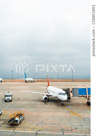 Planes parked at an airport during a cloudy day with ground service vehicles nearby Planes parked at an airport during a cloudy day with ground service vehicles nearby 138801601
