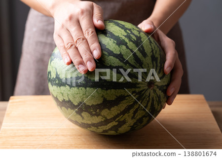 Woman's hands placing a fresh watermelon on a wooden cutting board, Tropical fruit in summer season 138801674