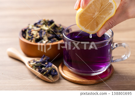 Hand squeezing lemon into a glass of blue butterfly pea tea to change color to purple Hand squeezing lemon into a glass of blue butterfly pea tea to change color to purple 138801695