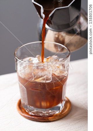 Pouring hot espresso from moka pot into a glass of ice cubes to make iced coffee Pouring hot espresso from moka pot into a glass of ice cubes to make iced coffee 138801706