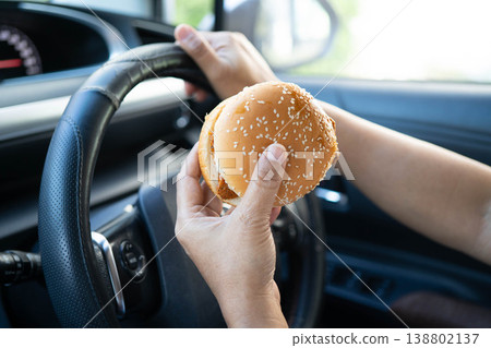 Asian woman driver hold and eat hamburger in car, dangerous and risk an accident. Asian woman driver hold and eat hamburger in car, dangerous and risk an accident. 138802137