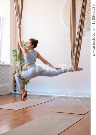Yoga training. Core strength. Young woman in sportswear doing exercise for leg hips muscle stability hanging in hammock in studio. Yoga training. Core strength. Young woman in sportswear doing exercise for leg hips muscle stability hanging in hammock in studio. 138802189