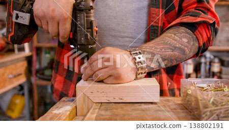Woodwork process. Screw driving. Mal carpenter hand with cordless power drill equipment assembling corner lumber plank on workbench. 138802191