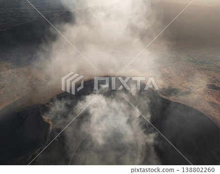 Volcano smoke rises above the landscape during the day near a crater Volcano smoke rises above the landscape during the day near a crater 138802260