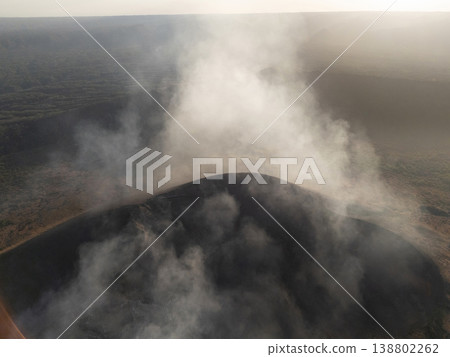 Smoke rises from volcanic site in remote landscape during sunset 138802262