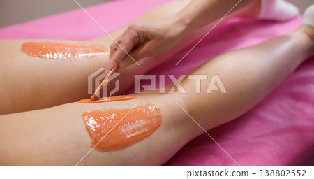 Wax depilation. Professional bodycare. Unrecognizable woman hands having hair removal procedure on legs in cosmetology beauty salon. Wax depilation. Professional bodycare. Unrecognizable woman hands having hair removal procedure on legs in cosmetology beauty salon. 138802352