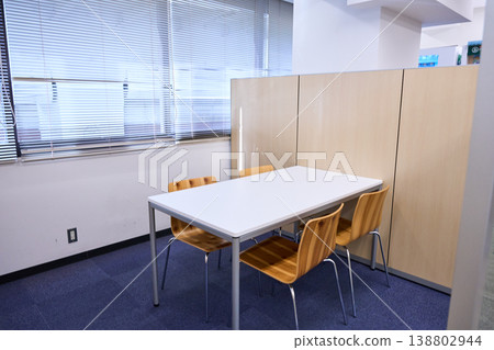 The office has a meeting space with a simple white table and wooden chairs. 138802944