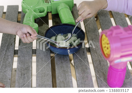 孩子們用湯匙從擺放著玩具槍的桌子上的碗裡舀冰淇淋。 孩子們用湯匙從擺放著玩具槍的桌子上的碗裡舀冰淇淋。 138803517