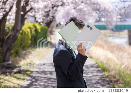 一名高中男生手捧一本書,走在櫻花盛開的路上。 一名高中男生手捧一本書,走在櫻花盛開的路上。 138803649