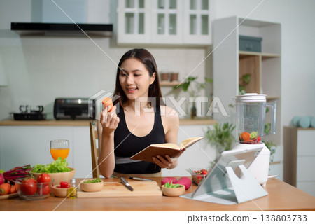 Asian woman reading recipe book while preparing fresh salad in home kitchen. Clean eating, nutrition planning, meal prep and healthy lifestyle concept. Asian woman reading recipe book while preparing fresh salad in home kitchen. Clean eating, nutrition planning, meal prep and healthy lifestyle concept. 138803733