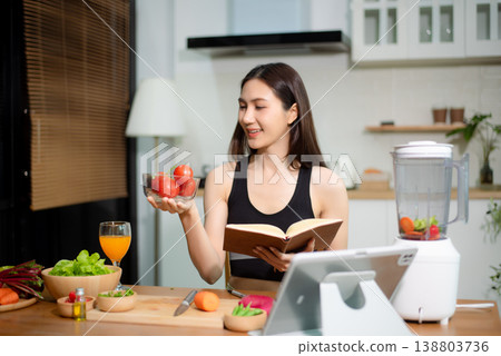 Asian woman reading recipe book while preparing fresh salad in home kitchen. Clean eating, nutrition planning, meal prep and healthy lifestyle concept. Asian woman reading recipe book while preparing fresh salad in home kitchen. Clean eating, nutrition planning, meal prep and healthy lifestyle concept. 138803736