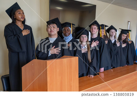 Graduates stand proudly at the ceremony with their hands over their hearts.  138803819