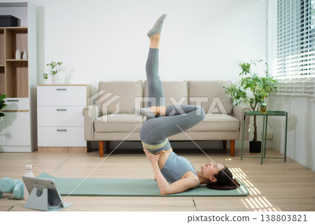 Asian woman stretching on yoga mat at home while following online workout. Home yoga, fitness exercise, flexibility training, wellness lifestyle, indoor healthy living. Asian woman stretching on yoga mat at home while following online workout. Home yoga, fitness exercise, flexibility training, wellness lifestyle, indoor healthy living. 138803821