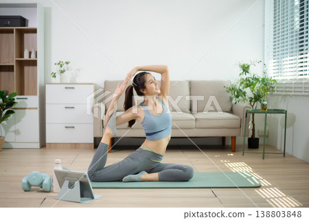 Asian woman doing yoga stretching on mat at home with online workout. Home fitness, flexibility training, wellness lifestyle, self care, indoor exercise. Asian woman doing yoga stretching on mat at home with online workout. Home fitness, flexibility training, wellness lifestyle, self care, indoor exercise. 138803848