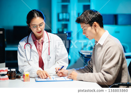 Asian female dentist explains dental model and treatment form to patient during consultation Asian female dentist explains dental model and treatment form to patient during consultation 138803860