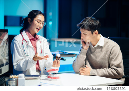 Dentist explaining tooth cleaning and oral hygiene using a dental model during consultation. Dentist explaining tooth cleaning and oral hygiene using a dental model during consultation. 138803891