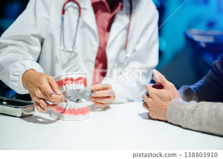 Dentist explaining oral hygiene using a dental model during consultation. Concept of dental care, tooth health, and professional healthcare 138803910