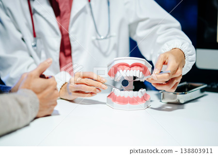 Dentist explaining oral hygiene using a dental model during consultation. Concept of dental care, tooth health, and professional healthcare Dentist explaining oral hygiene using a dental model during consultation. Concept of dental care, tooth health, and professional healthcare 138803911