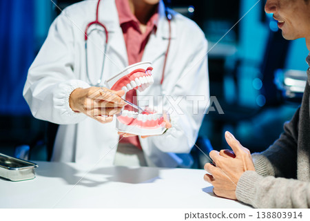 Dentist explaining tooth cleaning and oral hygiene using a dental model during consultation. Dentist explaining tooth cleaning and oral hygiene using a dental model during consultation. 138803914