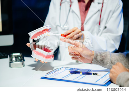 Asian female dentist holding dental model demonstrating brushing technique to young adult asian man patient Asian female dentist holding dental model demonstrating brushing technique to young adult asian man patient 138803934