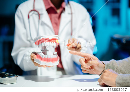 Asian female dentist holding dental model demonstrating brushing technique to young adult asian man patient Asian female dentist holding dental model demonstrating brushing technique to young adult asian man patient 138803937