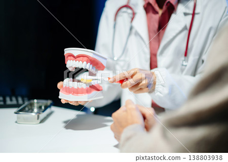 Asian female dentist holding dental model demonstrating brushing technique to young adult asian man patient Asian female dentist holding dental model demonstrating brushing technique to young adult asian man patient 138803938