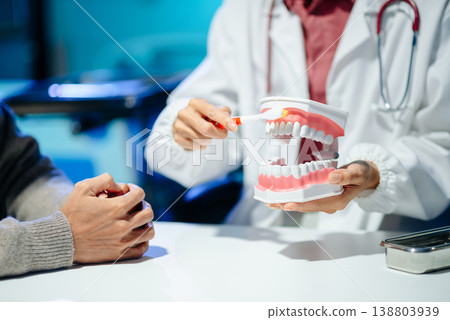 Dentist explaining oral hygiene using a dental model during consultation. Concept of dental care, tooth health, and professional healthcare Dentist explaining oral hygiene using a dental model during consultation. Concept of dental care, tooth health, and professional healthcare 138803939