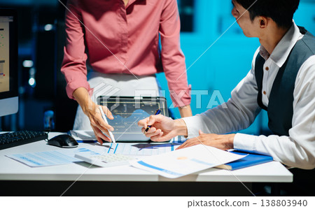 Business documents on office table with smart phone and laptop and two colleagues discussing data in the background 138803940