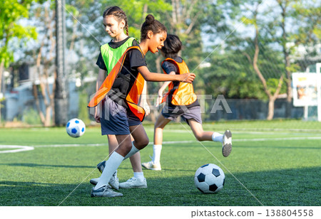 Two young girls and a boy play a competitive soccer game on the green grass of a park, kicking the ball in an action-packed team sport activity Two young girls and a boy play a competitive soccer game on the green grass of a park, kicking the ball in an action-packed team sport activity 138804558