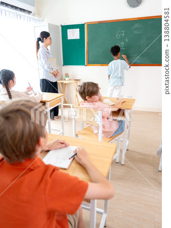Vertical image of the teacher tell African American boy try to write the answer for calculation question on blackboard in front of classroom. Vertical image of the teacher tell African American boy try to write the answer for calculation question on blackboard in front of classroom. 138804581