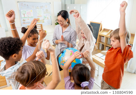 High view of teacher give the question about country on earth and tell the kids to answer and the children raise their hands to compete for answer using model globe. High view of teacher give the question about country on earth and tell the kids to answer and the children raise their hands to compete for answer using model globe. 138804590