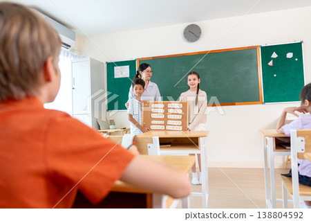 Back of the boy sit in the classroom and look to the front of class that boy and girl present about multiplication table and teacher stand beside of them. Back of the boy sit in the classroom and look to the front of class that boy and girl present about multiplication table and teacher stand beside of them. 138804592