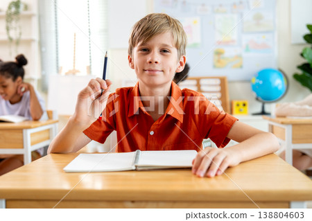 Portrait of mix-raced boy with blond hair hold a pencil and look at camera with little smile during he study in the classroom. Portrait of mix-raced boy with blond hair hold a pencil and look at camera with little smile during he study in the classroom. 138804603