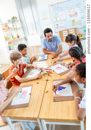Vertical image of the teacher stay on head of the table and explain about draw and paint classroom during the children witll start to create their working. Vertical image of the teacher stay on head of the table and explain about draw and paint classroom during the children witll start to create their working. 138804617