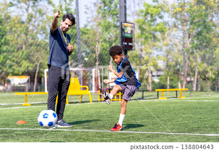 Coach point to the direction of shooting and the African American boy kick the boy to that direction during practice in the field. Coach point to the direction of shooting and the African American boy kick the boy to that direction during practice in the field. 138804643
