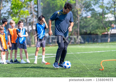 Coach show and guide the children to dribble the ball pass through obstacle in the field to practice and prepare for the competition. Coach show and guide the children to dribble the ball pass through obstacle in the field to practice and prepare for the competition. 138804655