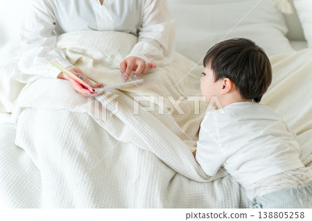 Mother reading a picture book to her child in bed (putting to sleep, nap, reading aloud) Mother reading a picture book to her child in bed (putting to sleep, nap, reading aloud) 138805258